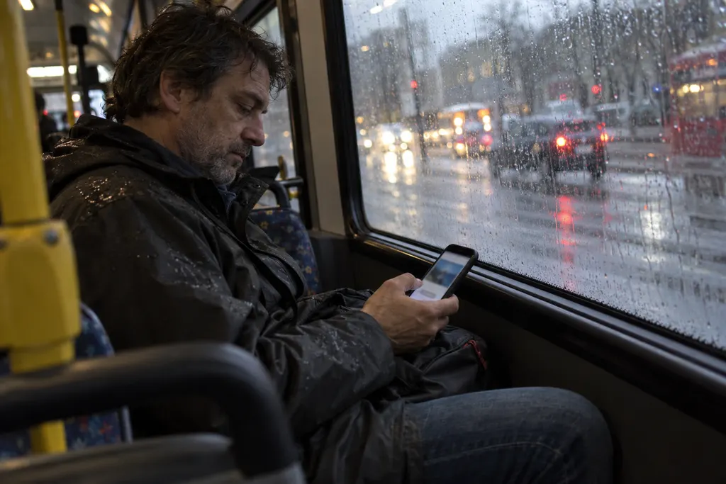 A man on a bus glancing at a landing page on his phone, thumb already near the edge of the screen